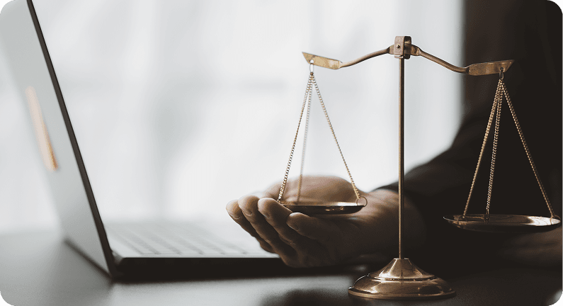 A hand beside a balance scale in front of an open laptop