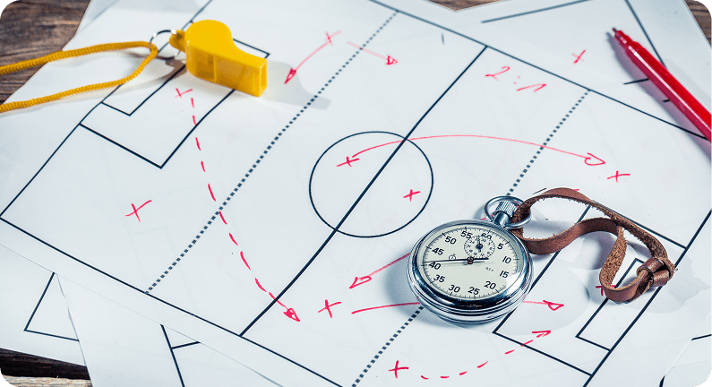 A stopwatch and whistle on a tactics board marked with plays